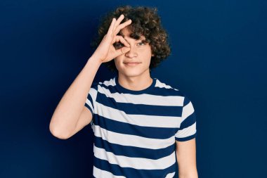 Yakışıklı, çizgili tişört giyen, el hareketleriyle gülümseyen, mutlu yüzüyle parmaklarının arasından bakan genç adam.. 