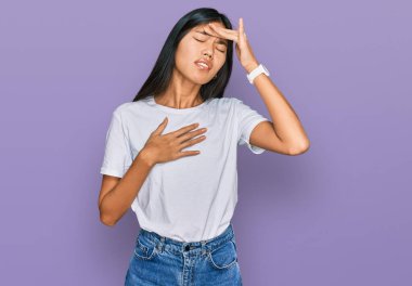 Güzel, beyaz tişört giyen Asyalı genç bir kadın hastalık, ateş, grip ve virüs yüzünden alnına dokunuyor. 