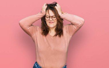 Genç ve cüsseli bir kadın gündelik kıyafetler giyiyor ve gözlük takıyor. Baş ağrısı çekiyor, çaresiz ve stresli. Çünkü ağrı ve migren ağrısı var. Eller başının üstünde.. 