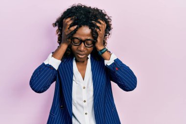 Genç Afro-Amerikalı kadın iş kıyafetleri ve gözlük takıyor. Baş ağrısı çekiyor, çaresiz ve stresli. Çünkü acı ve migren. Eller başının üstünde.. 