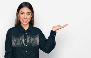 Gündelik kıyafetler giyen genç İspanyol kadın neşeli bir şekilde gülümsüyor ve avuç içiyle kameraya bakıyor.. 