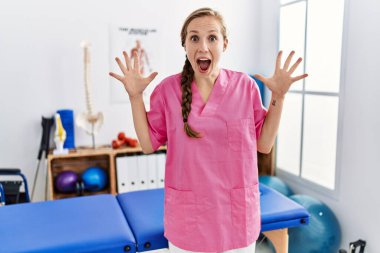 Ağrı giderme kliniğinde çalışan genç sarışın kadın zaferi mutlu bir gülümseme ve ellerini kaldırarak kazanan ifadeyle kutluyor. 