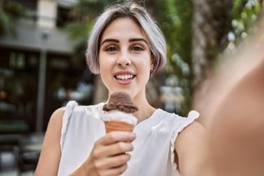 Kafkasyalı genç bir kız dondurma yiyor ve şehrin kamerasının önünde selfie çekiyor..