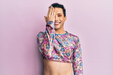 Makyaj yapan yakışıklı bir adam. Moda kıyafetleri giyiyor. Bir gözünü eliyle kapatıyor.. 