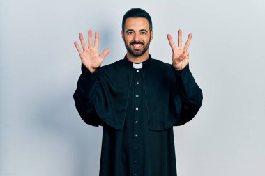 Sakallı, Katolik rahip cüppeli yakışıklı bir adam. Sekiz numaralı parmaklarıyla kendini beğenmiş ve mutlu gülümserken onu işaret ediyor.. 