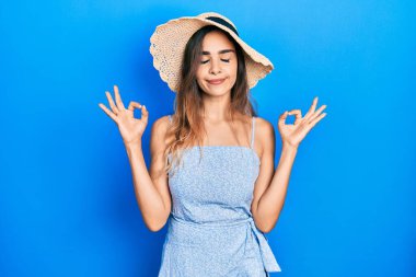 Genç İspanyol kız yaz şapkası takıyor rahatlıyor ve gözleri kapalı gülümsüyor parmaklarıyla meditasyon hareketi yapıyor. yoga konsepti. 