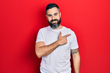 Gündelik beyaz tişört giyen genç İspanyol adam. Gülümsüyor, elleri ve parmakları yana doğru uzanıyor. 