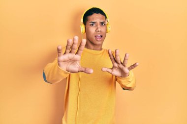 Genç Afro-Amerikalı adam kulaklık takıp müzik dinliyor. Korkudan dehşete düşmüş ve korkmuş. El hareketlerini durdur, şok içinde bağır. panik konsepti. 