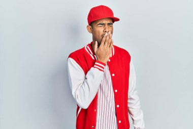 Beyzbol üniforması giyen genç Afro-Amerikan adam ağız ve ağızla esnemekten sıkılmış. Huzursuz ve uykulu.. 