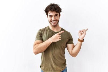 İspanyol adam izole edilmiş beyaz arka planda duruyor gülümsüyor ve kameraya bakıyor iki eliyle ve parmaklarıyla kenarı işaret ediyor.. 