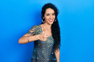 Bindi ve geleneksel kurta elbisesi giyen genç bir kadın elleriyle mutlu bir jest yapıyor. Kameraya bakıp başarıyı gösteren ifade. 