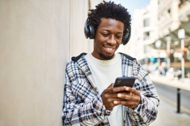 Afro saçlı, kulaklık takan ve akıllı telefon kullanarak müzik dinleyen yakışıklı bir zenci.