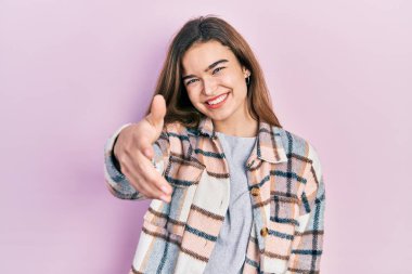 Gündelik kıyafetler giymiş genç beyaz bir kız gülümseyerek selamlama ve hoş geldin demek için el sıkışmayı teklif ediyor. başarılı iş. 