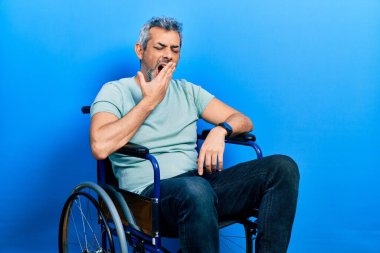 Gri saçlı, tekerlekli sandalyede oturan yakışıklı, orta yaşlı bir adam. Ağzını eliyle kapatmaktan sıkılmış. Huzursuz ve uykulu.. 