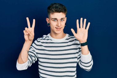 Kulakları genişlemiş, sıradan çizgili tişörtler giyen genç beyaz çocuk yedinci parmaklarını gösterirken kendine güvenen ve mutlu bir şekilde gülümsüyor.. 