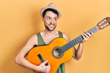 Latin kökenli genç adam klasik gitar çalıyor gülümsüyor, yan tarafa bakıyor ve düşünüyor.. 