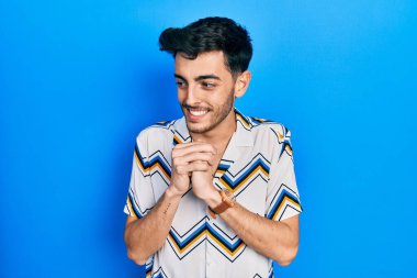 Gündelik kıyafetler giyen genç İspanyol adam gergin ve heyecanlı, elleri çenesinde yan tarafa bakıyor. 