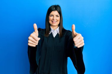 Yargıç üniforması giyen genç İspanyol kadın elleriyle olumlu jest yapmayı onaylıyor. Gülümsüyor ve başarı için seviniyor. kazanan jest. 