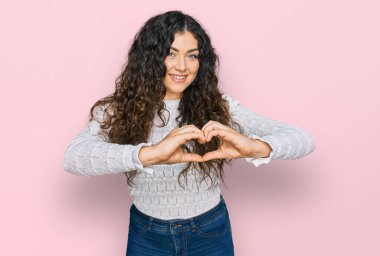 Gündelik giysiler giyen genç İspanyol kız. Sevgiyle gülümseyen. Elleriyle kalp sembolü ve şekli gösteren. romantik kavram. 