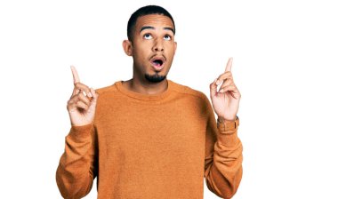 Gündelik giysiler giyen genç Afro-Amerikan adam şaşkın ve şaşırmış bir şekilde yukarı baktı ve parmaklarıyla işaret etti ve kollarını kaldırdı.. 