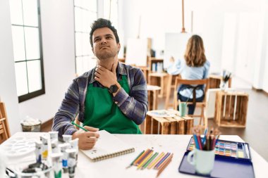 Sanat stüdyosundaki genç sanatçı ağrılı boyuna dokunuyor. Grip, mantar ve enfeksiyon yüzünden boğazı ağrıyor. 