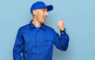 Sakallı, inşaatçı tulumu giyen, mutlu yüzüyle gülümseyen ve baş parmağıyla yüzünü gösteren kel bir adam.. 