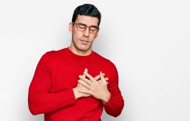 Yakışıklı İspanyol bir adam günlük kıyafetler ve gözlük takıyor elleri göğsünde, gözleri kapalı gülümsüyor ve yüzünde minnet ifadesi var. sağlık kavramı. 