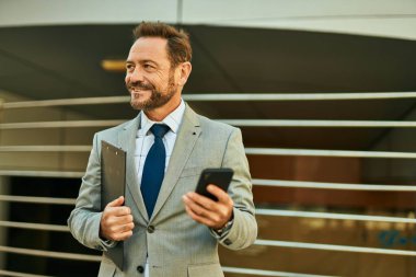 Şehirdeki akıllı telefondan gülümseyen orta yaşlı bir işadamı..