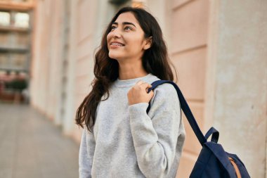 Genç ortadoğulu kız gülümseyerek şehirde mutlu mesut duruyor..