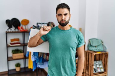 Alışveriş torbaları tutan sakallı yakışıklı genç adam perakende dükkanında komik suratıyla yanaklarını şişiriyor. Havayla şişmiş ağız, çılgın bir ifade.. 