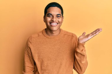 Genç, yakışıklı, sıradan bir kazak giyen neşeli bir şekilde gülümseyen ve avuç içi kameraya bakan İspanyol bir adam.. 