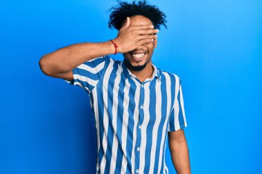 Sakallı, sıradan çizgili tişörtlü, gülümseyen ve gülen genç Afro-Amerikan bir adam şaşırtmak için gözlerini kapatıyor. kör kavram. 