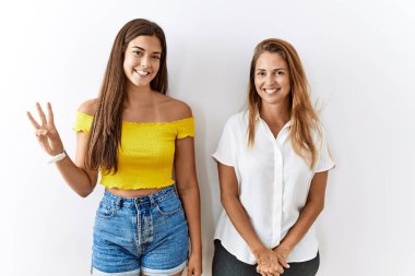 Anne ve kızı birlikte izole edilmiş arka planda duruyorlar. Üç numarayı gösteriyorlar ve gülümsüyorlar. Kendinden emin ve mutlular.. 