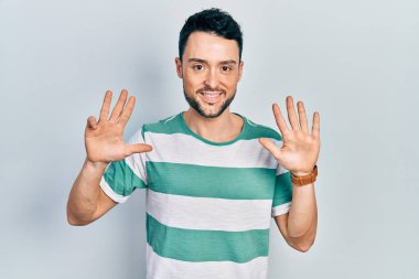 Gündelik kıyafetler giyen genç İspanyol adam dokuz numarayı gösterip işaret ederken kendinden emin ve mutlu bir şekilde gülümsüyor.. 