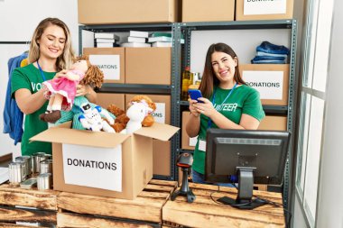 Yardım merkezinde çalışmaktan mutlu gülümseyen iki genç gönüllü kadın. Akıllı telefon kullanan mutlu bir kız..