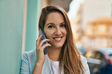 Genç sarışın iş kadını gülümsüyor. Şehirdeki akıllı telefondan konuşuyor..