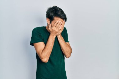 Ağlarken suratını ellerle kapatan günlük beyaz tişört giyen genç bir İspanyol. depresyon kavramı. 