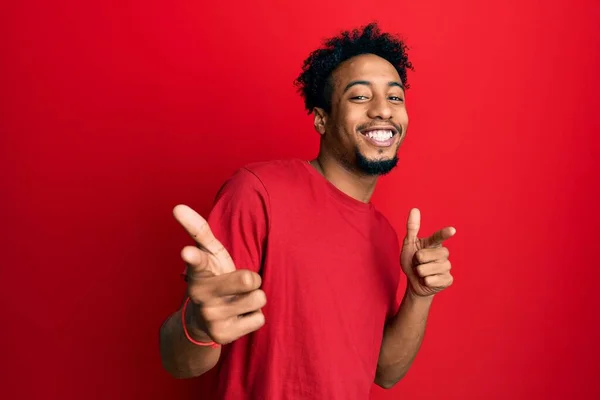 ひげを生やした若いアフリカ系アメリカ人の男性は 幸せと面白い顔をしたカメラに指を指してカジュアルな赤いTシャツを着ていました 良いエネルギーと振動は — ストック写真