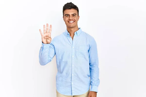 自信と幸せ笑顔ながら 孤立した背景を示すと指の数4で指摘し ビジネスシャツを身に着けている若いヒスパニック系の男 — ストック写真