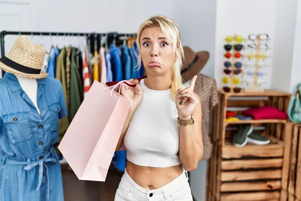 若いですCaucasian女性保持ショッピングバッグで小売店上を指している悲しいと動揺 指で方向を示す 不幸と落ち込んで — ストック写真