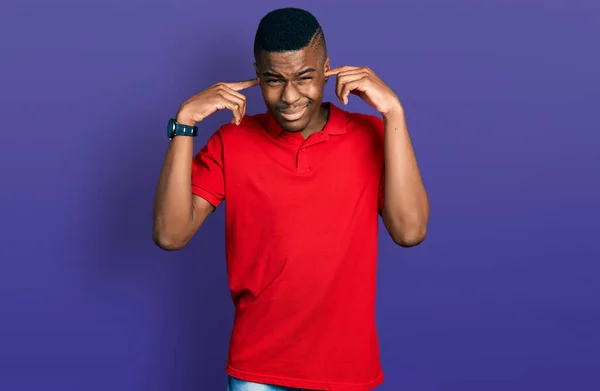 年轻的非洲裔美国人穿着休闲的红色T恤 用手指捂住耳朵 对嘈杂的音乐感到恼怒 聋人概念 — 图库照片