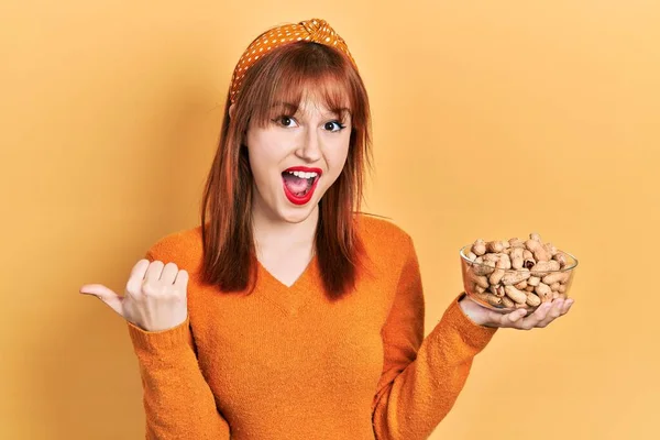 Redhead Young Woman Holding Peanuts Pointing Thumb Side Smiling Happy — Stock Photo, Image