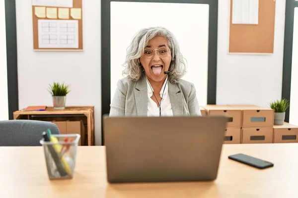 中年女商人坐在办公桌前工作 在办公室里用笔记本电脑伸出舌头 带着滑稽的表情高兴极了 情感概念 — 图库照片