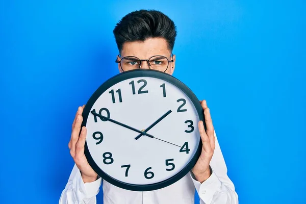 Joven Hombre Hispano Sosteniendo Gran Reloj Sobre Cara Escéptico Nervioso — Foto de Stock