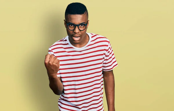 若いアフリカ系アメリカ人の男性が怒って怒っていると怒って怒って怒って怒って叫びながら拳を上げるカジュアルTシャツを着て 怒りと攻撃的な考え方 — ストック写真