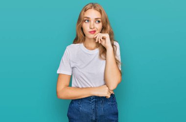 Beyaz gündelik tişört giyen genç beyaz kız ciddi yüz ifadesiyle eli çenesinde soruyu düşünüyor, kafa karıştırıcı bir fikir hakkında düşünceli. 