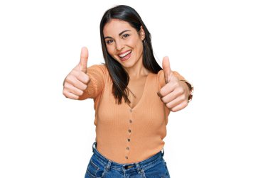 Latin kökenli genç bir kadın, günlük giysiler giyip, olumlu jestler yapıyor, gülümsüyor ve başarı için seviniyor. kazanan jest. 