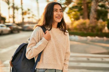 Genç ortadoğulu kız gülümseyerek şehirde mutlu mesut duruyor..