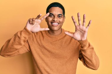 Genç, yakışıklı, sıradan bir süveter giyen, 8 numaralı parmaklarını gösterip, gülümseyen, kendinden emin ve mutlu bir İspanyol.. 