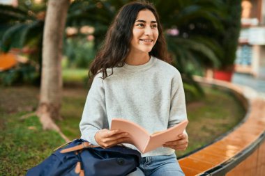 Genç ortadoğu öğrencisi kız şehirde mutlu bir şekilde kitap okuyor.